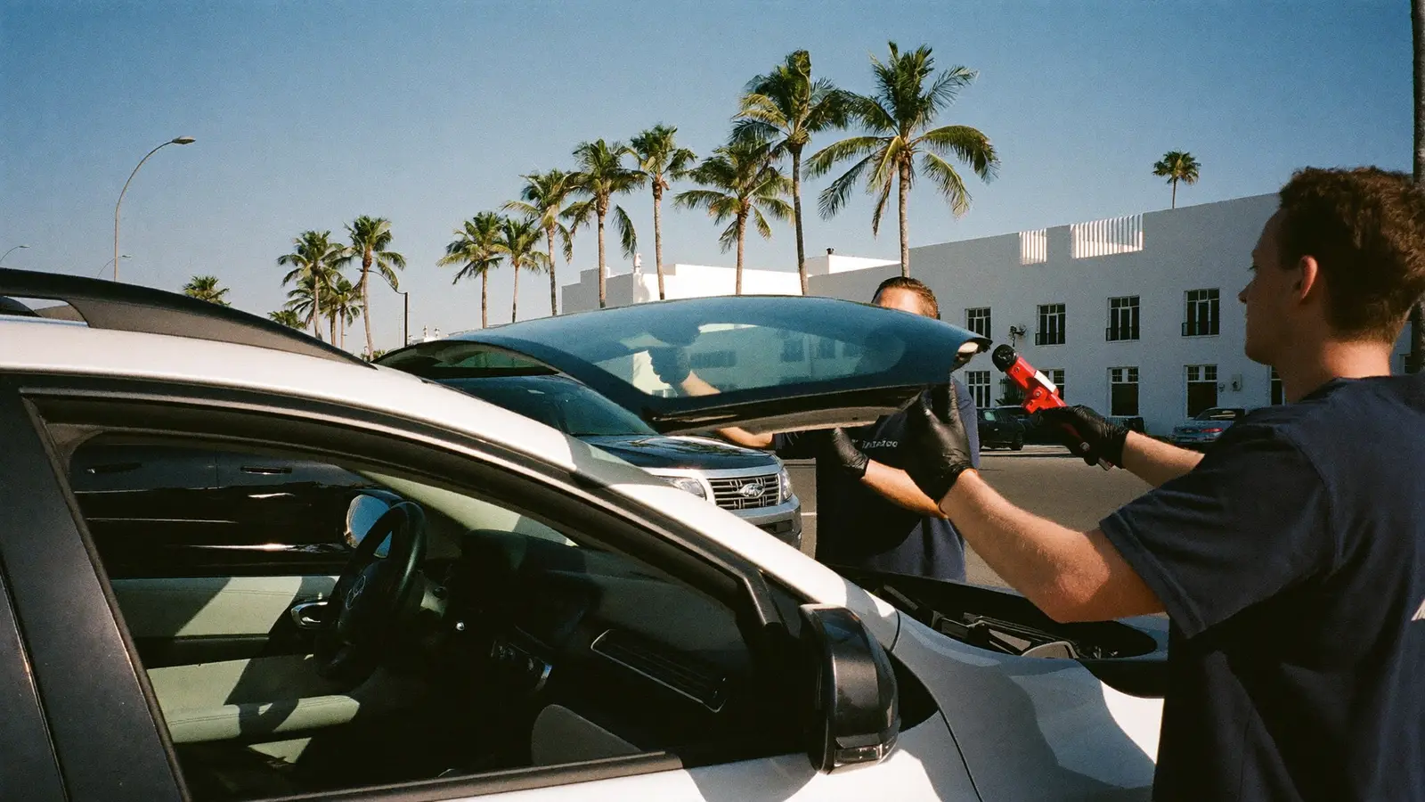 Two technicians setting a new windshield on an SUV in a sunny parking lot